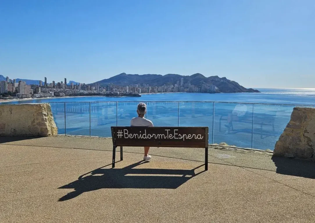 Woman sitting on bench overlooking the resort of Benidorm.